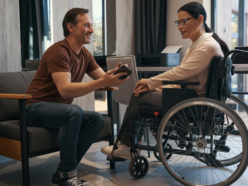 Jolly man with smartphone in office with female with disability