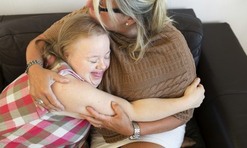 Mother and daughter with down syndrome embracing on sofa